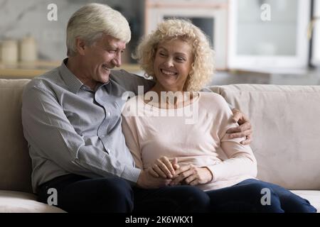 Attractive loving older couple talking seated on couch Stock Photo