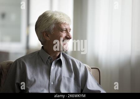 Pensive senior man relaxing on couch smile looking into distance Stock Photo