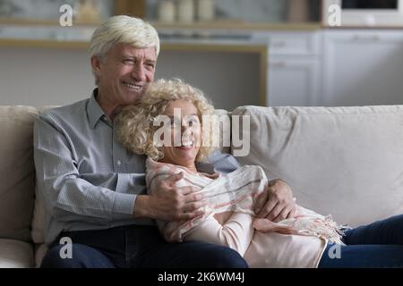 Attractive loving older spouses resting together on comfortable sofa Stock Photo