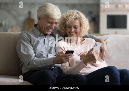 Positive mature spouses spend time using two modern smartphones Stock Photo