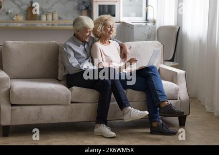 Happy retired spouses spend leisure using laptop Stock Photo