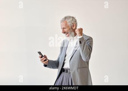 Excited happy old business man investor raising fist using smartphone. Stock Photo