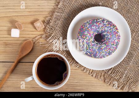 Donut with colorful sprinkles and cup of coffee on wooden table close-up Stock Photo