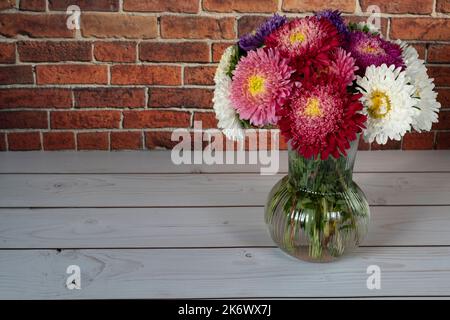 Beautiful bouquet of asters on white wooden table in front of brick wall Stock Photo