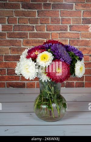 Beautiful bouquet of asters on white wooden table in front of brick wall Stock Photo