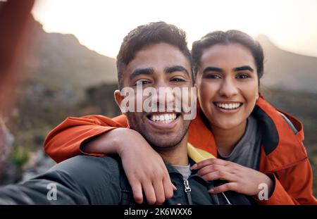 We love hiking. Cropped portrait of an affectionate young couple taking selfies while hiking in the mountains. Stock Photo