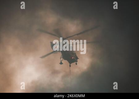 A fire helicopter carries a container of water to extinguish a fire in a production building Stock Photo