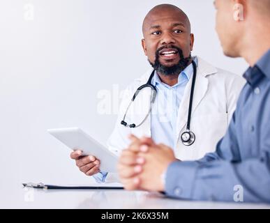Lets talk about it. a mature male doctor using a digital tablet during a consultation at a clinic. Stock Photo