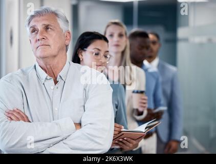 How much longer do I have to wait. a mature businessman standing with his arms crossed while waiting in line in an office. Stock Photo