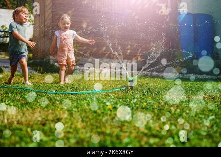Two children have fun in the garden - playing with water on lawn Stock Photo