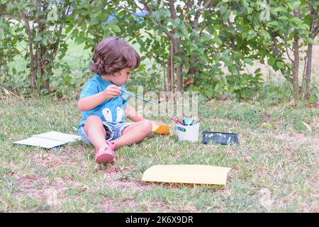 Cute boy doing homework laying on grass. Child reading a book in the summer park. Concept of kids learning, study, outdoors in the park. Stock Photo