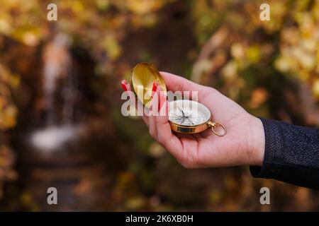 Closeup of woman tourist hand holding old magnetic compass in the forest. Waterfall on the background. Stock Photo