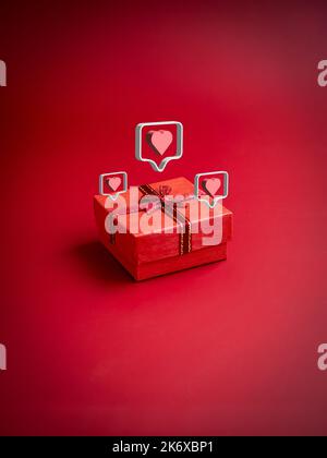 3d love like heart icons floating on small red present gift box with ribbon on red background, vertical style. Essential gift on special days, birthda Stock Photo