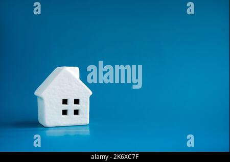 A simple miniature ceramic white house model on blue background with copy space, minimal style. Concepts of residential or real estate property, land Stock Photo