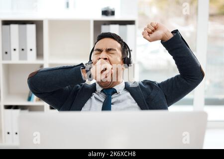 Give your body the break it deserves. a young male call center agent yawning while working in an office. Stock Photo