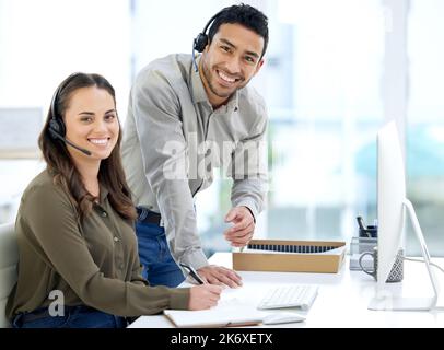 Teamwork makes the sales target work. a businessman and businesswoman using a headset and computer while working in a modern office. Stock Photo
