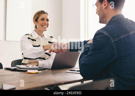 Excited HR manager shaking hands with a successful job candidate during an interview. Happy businesswoman hiring a new employee in her office. Cheerfu Stock Photo