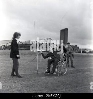 1964, historical, a disabled young man sitting in a wheelchair, attempting to throw the javelin outside on the sports ground of Stoke Mandeville Hospital, Aylesbury, Bucks, England, UK. The hospital was the home of the National Spinal Injuries Centre and in 1948 after WW2, the Stoke Mandeville Games was started for injured ex-serviceman, which was the forerunner of the modern Paralympics. Stock Photo