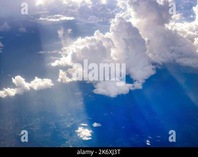 Aerial view flying above dramatic fluffy clouds and sun rays piercing shining through the clouds, sunny cloudscape, sunlight, Traveling by air Stock Photo