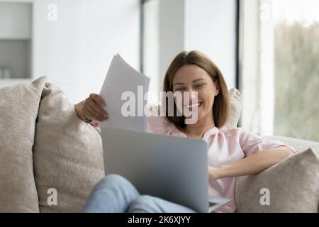 Woman holds papers sit on sofa with computer on laps Stock Photo