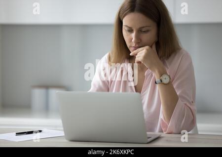 Serious pensive freelancer woman working on laptop Stock Photo