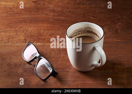 Brewed milk coffee and reading glasses on a wooden table Stock Photo