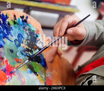 Close up of man's hand mix paints with brush in palette and painting still life picture on canvas in artist studio. Stock Photo