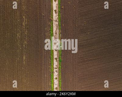 Aerial view dirt road made of concrete divides field with wet fertile land Stock Photo