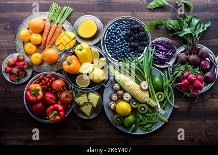 Various fresh organic fruits and vegetables on metal plates in rainbow colours against a dark wooden background. Stock Photo