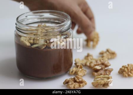 Chocolate walnut custard. Chocolate custard served with crushed walnuts. A quick and easy dessert, served in a glass bottle. Shot on white background Stock Photo