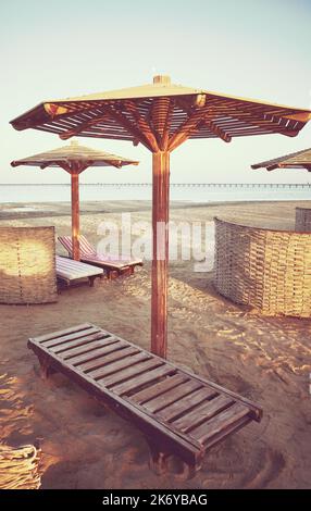 Wooden sun umbrellas, sunbeds and windscreens on beach, color toning applied, Marsa Alam, Egypt. Stock Photo