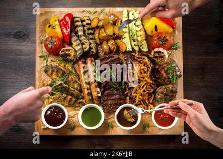 A board with grilled appetizers and sauces. Grilled vegetables and meat snacks: sausages, chicken fillets, pork and beef steaks. Stock Photo