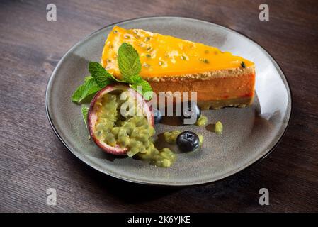 Passion fruit cheesecake. A delicate dessert portion with fresh passionfruit wedges and blueberries on a plate. The dessert is sprinkled with powdered Stock Photo