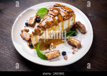 Caramel-flavored cheesecake. A slice of dessert topped with salted caramel syrup, peanuts and milk chocolate. The cheesecake is garnished with blueber Stock Photo