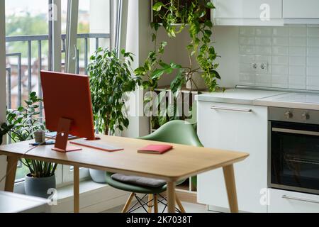 Cozy home office for freelancer with stylish red monitor on table near with large kitchen window Stock Photo