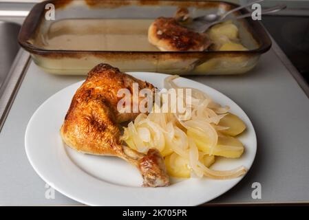 Chicken thigh with potatoes and onion on a plate with the tray in the background fresh from the oven. Stock Photo