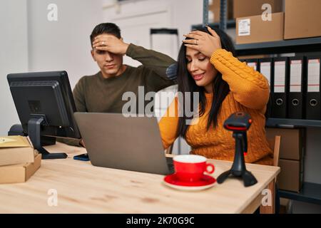 Young woman and man working at small business ecommerce stressed and frustrated with hand on head, surprised and angry face Stock Photo