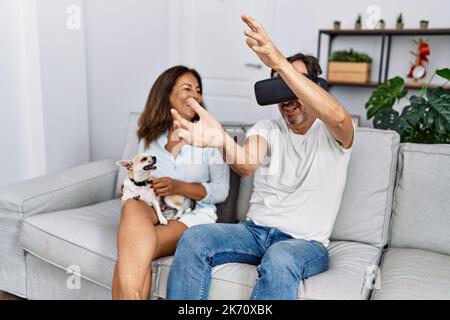 Middle age man and woman couple using vr goggles sitting on sofa with dog at home Stock Photo