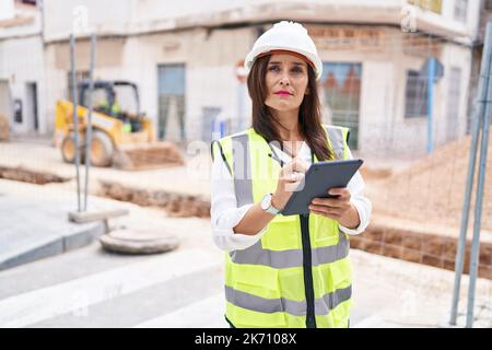 Young beautiful hispanic woman architect drawing on touchpad with relaxed expression at street Stock Photo