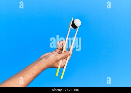 Hand of man holding sushi with chopsticks over isolated blue background Stock Photo