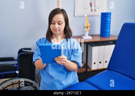 Down syndrome woman wearing physiotherapy uniform using touchpad at physiotherapist clinic Stock Photo