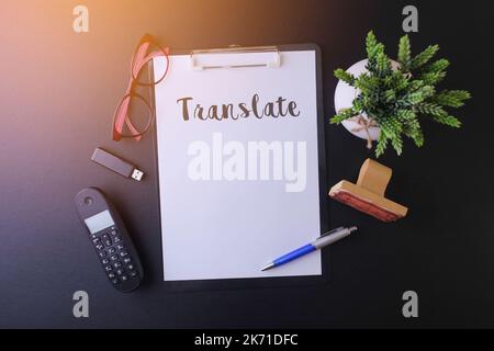 Notebook writing "Translate " on table, Working space at the office with cell phone ,usb drive,glasses and green plant Stock Photo