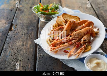 From above delicious king prawns served on plate near bowls of sauce and fresh salad on wooden table during dinner in restaurant Stock Photo