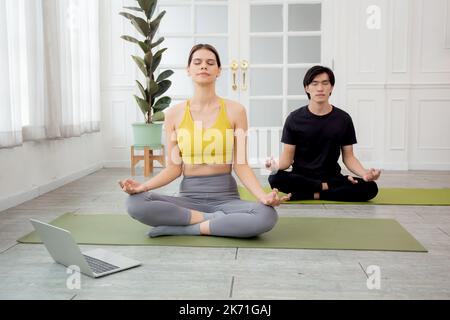 Young woman and man practicing yoga with watching laptop computer and meditating for relaxation at home, couple training yoga and exercise for bodycar Stock Photo