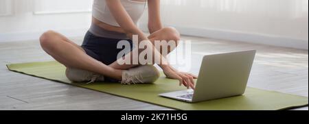 Young woman practicing exercise or yoga on mat while watching laptop computer tutorial online at home, woman having motivation looking notebook for wo Stock Photo