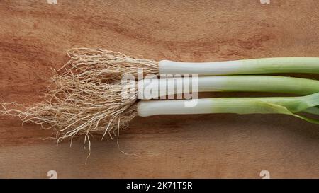 close-up of leeks with roots, freshly harvested edible raw vegetable on a cutting board background, taken from above with Stock Photo