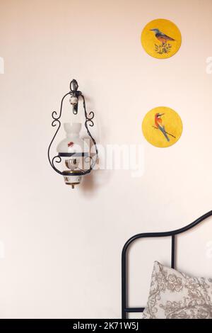 The interior of an old building, a room with a lamp by the bed and drawings of birds. Vertical photo. Stock Photo
