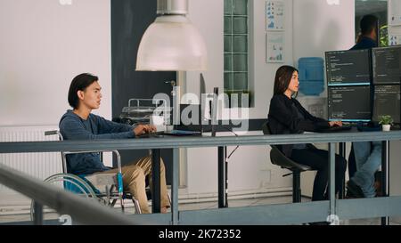 Software programer with physical disability writing code on computer, displaying artificial intelligence algorithm. Developer in wheelchair coding database online cloud computing. Stock Photo