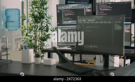 Empty desk with multiple monitors displaying server code and programming language, compiling in software developing agency office. System cloud computing online database algorithms. Stock Photo