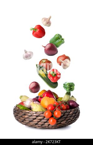 Many healthy vegetables falling into wicker basket on white background Stock Photo
